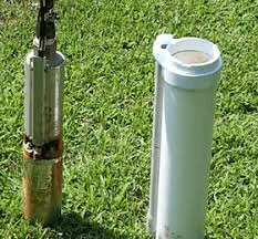 A water pump is sitting next to a white pipe in the grass