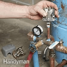 A person is holding a pressure switch next to a water tank