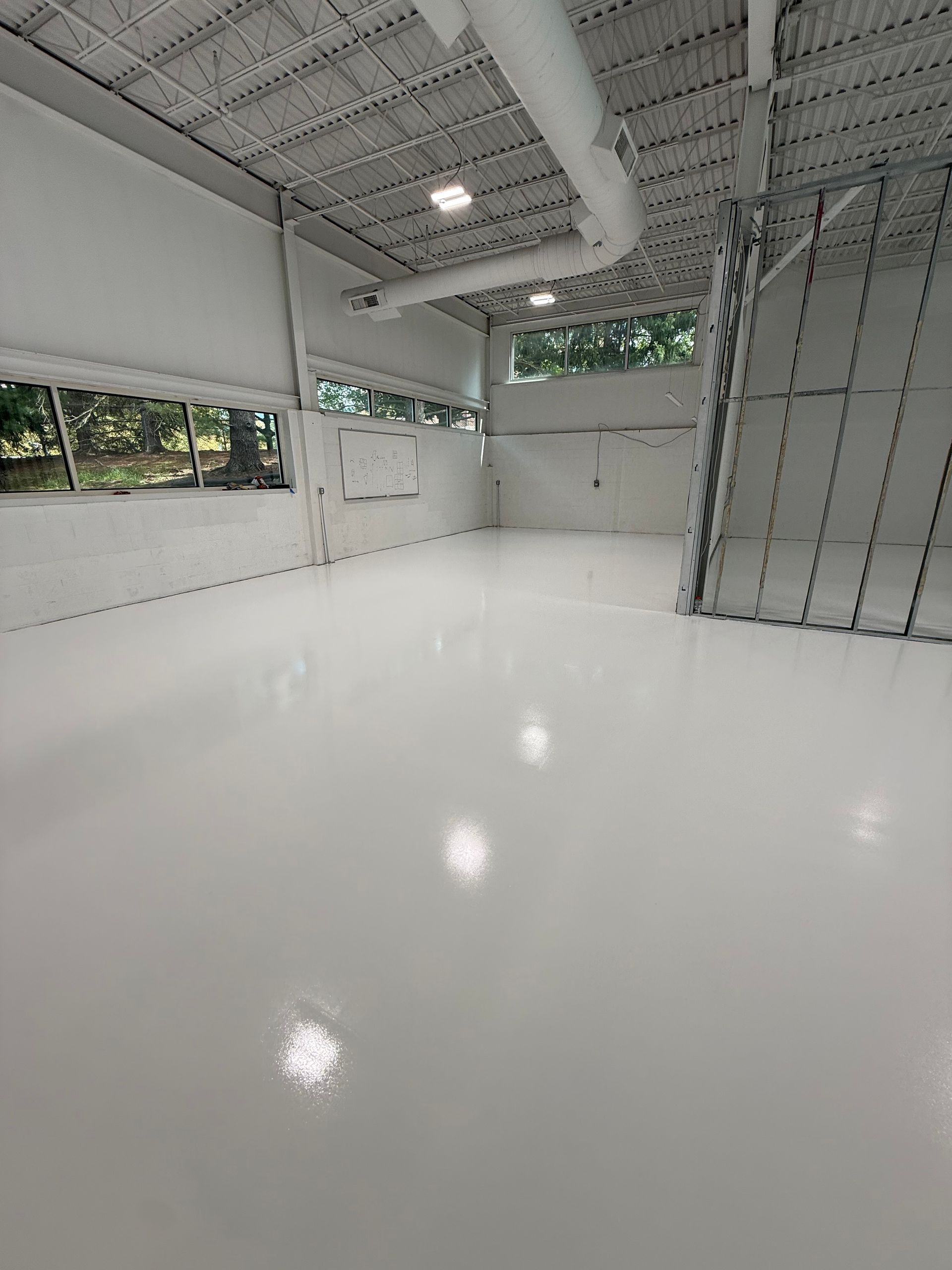 Empty modern industrial room with glossy white floor, exposed ceiling, and large windows