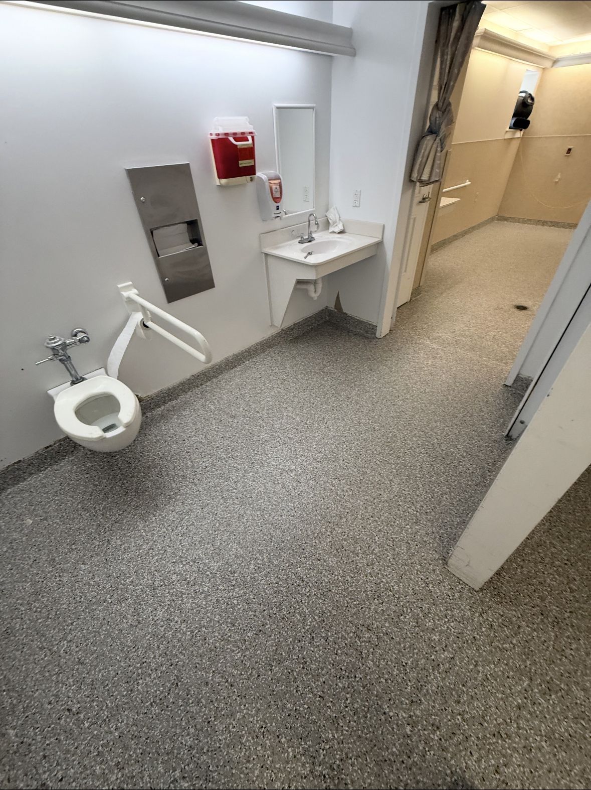 Accessible restroom with toilet, sink, grab bars, and open doorway to shower area