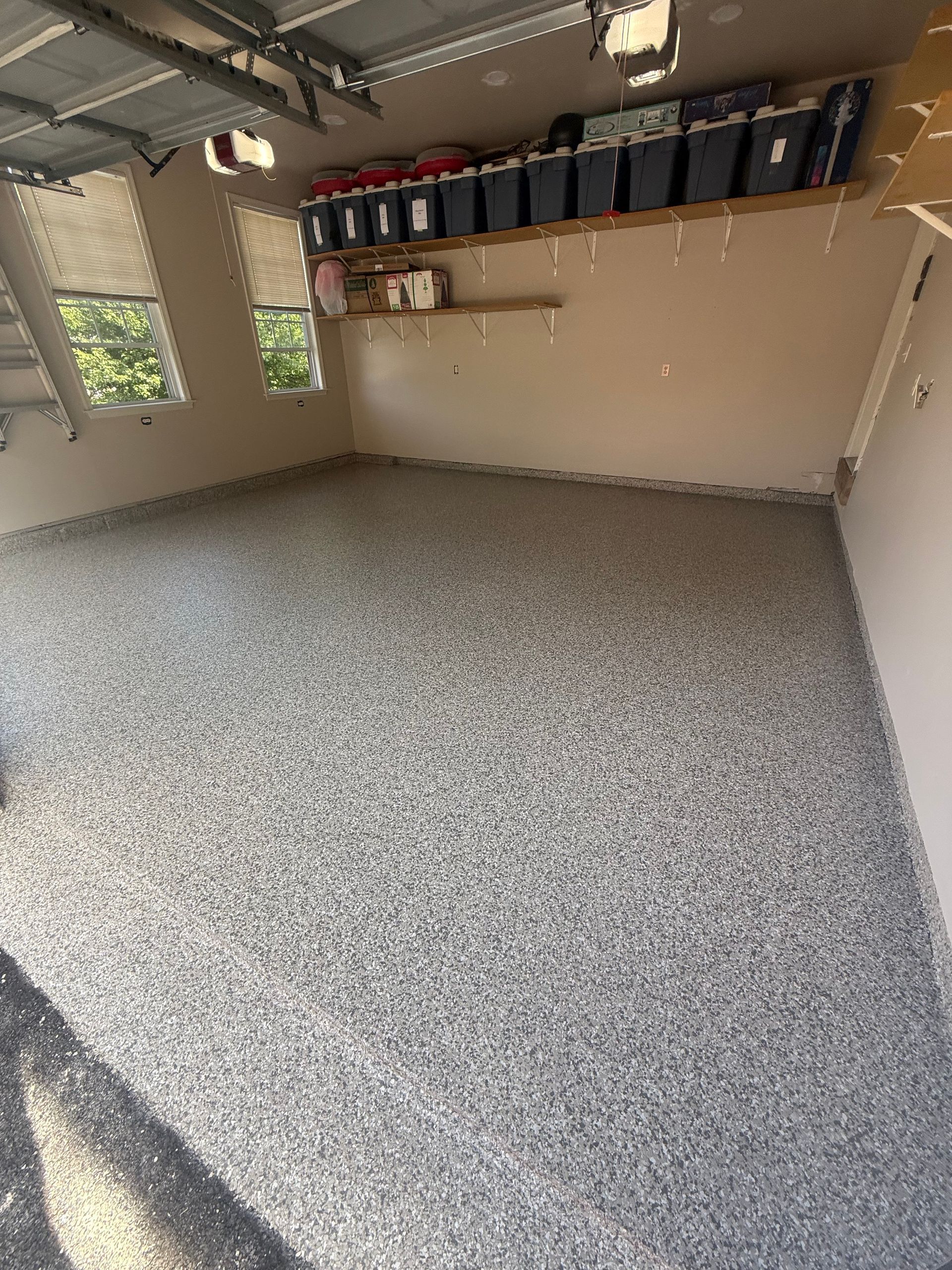 Empty garage with speckled floor, beige walls, ceiling lights, and storage bins on wall shelves.