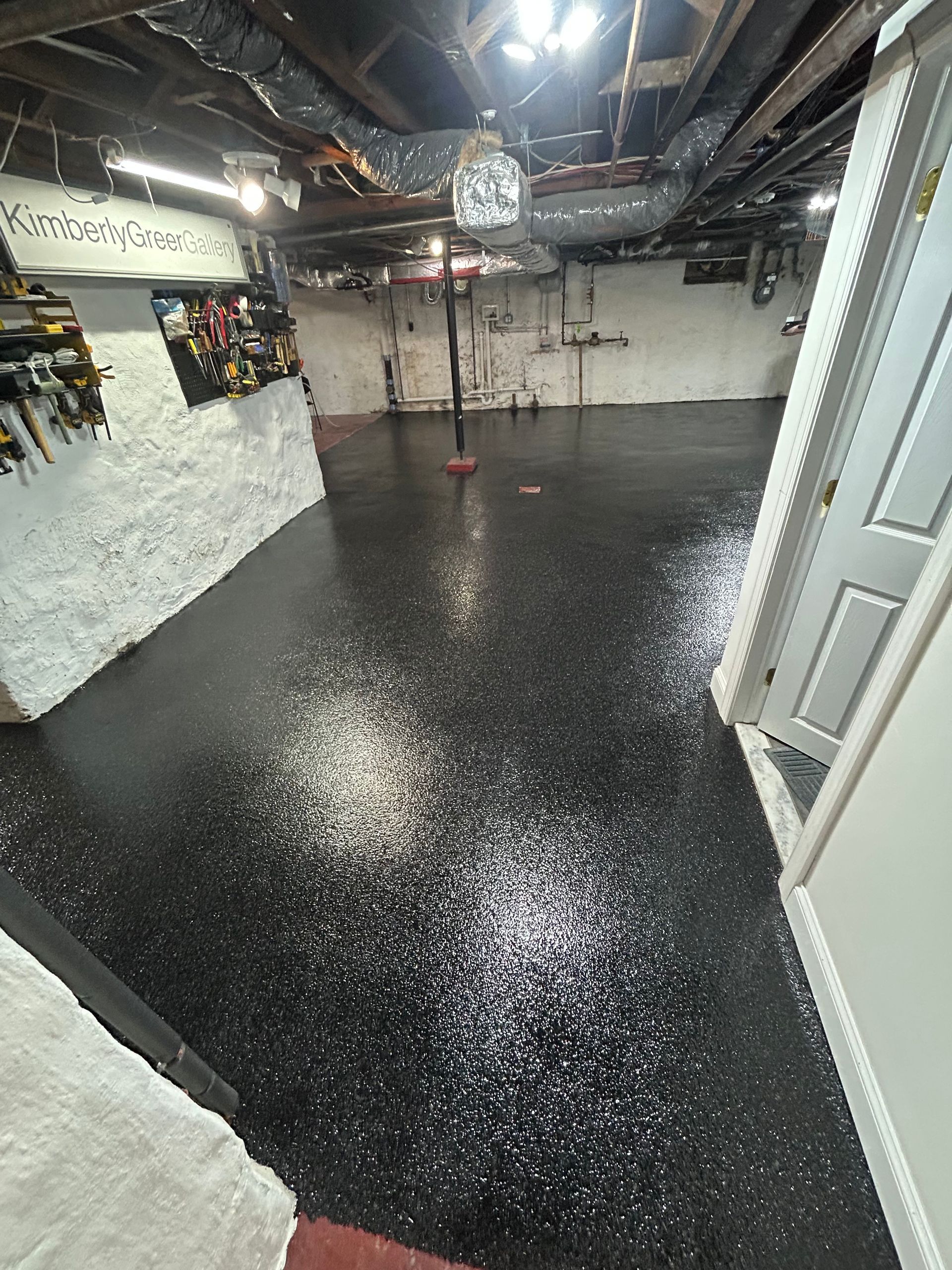 Empty basement room with glossy black floor, white walls, exposed ceiling, and bright overhead lights