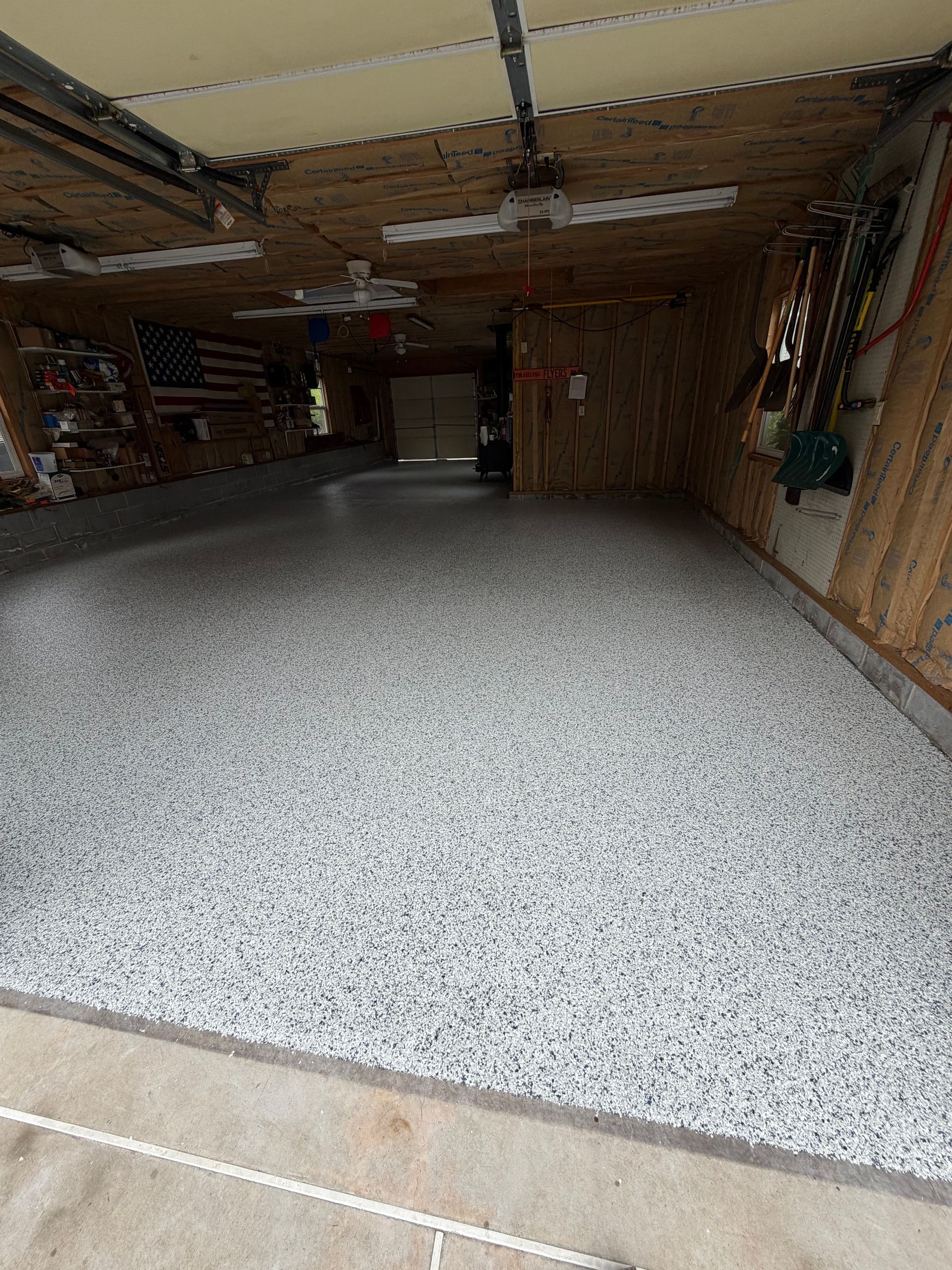 Spacious garage with a speckled epoxy floor, wooden walls, and storage shelves along the sides