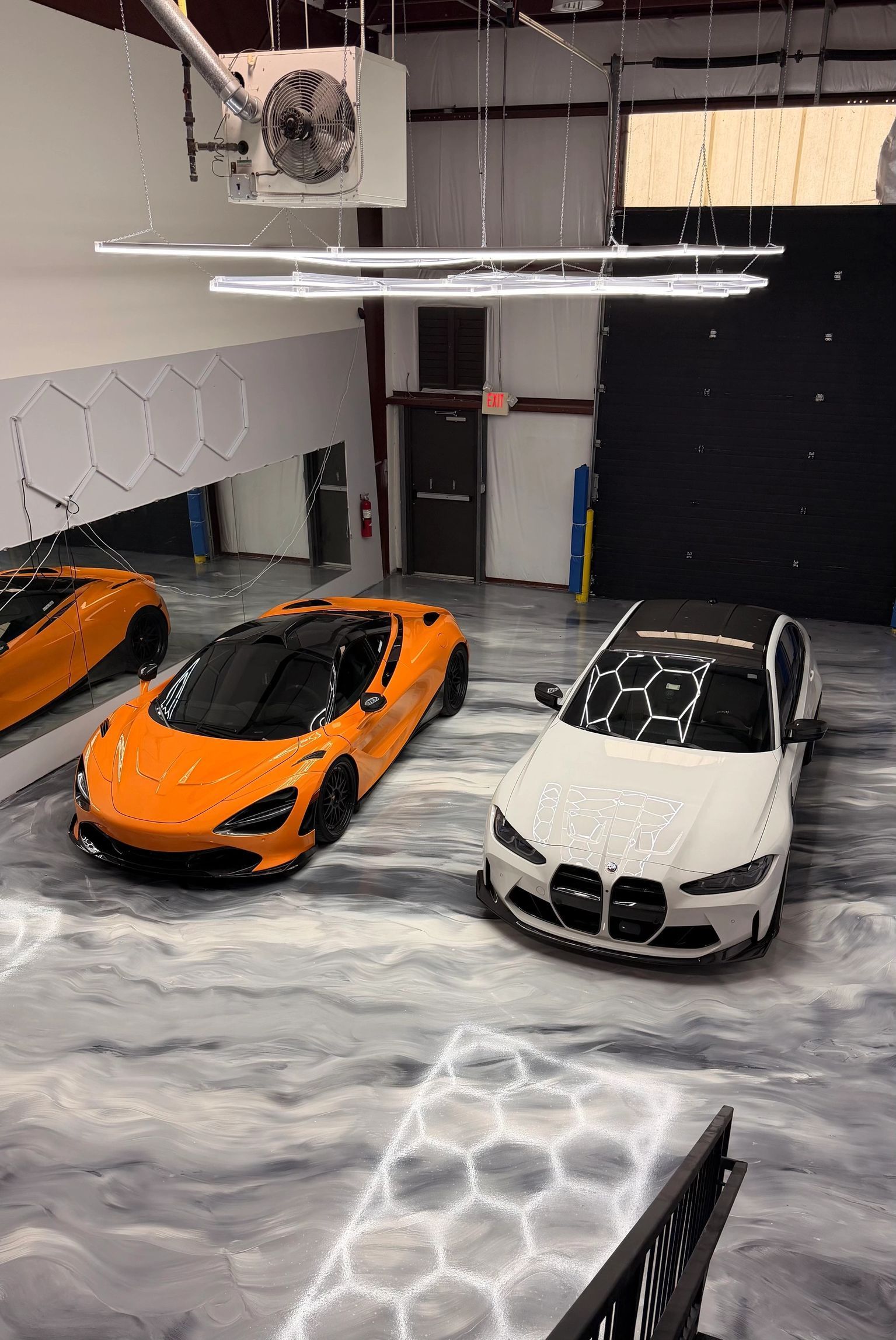 Two sports cars, orange and white, parked in a garage with a basketball hoop overhead.