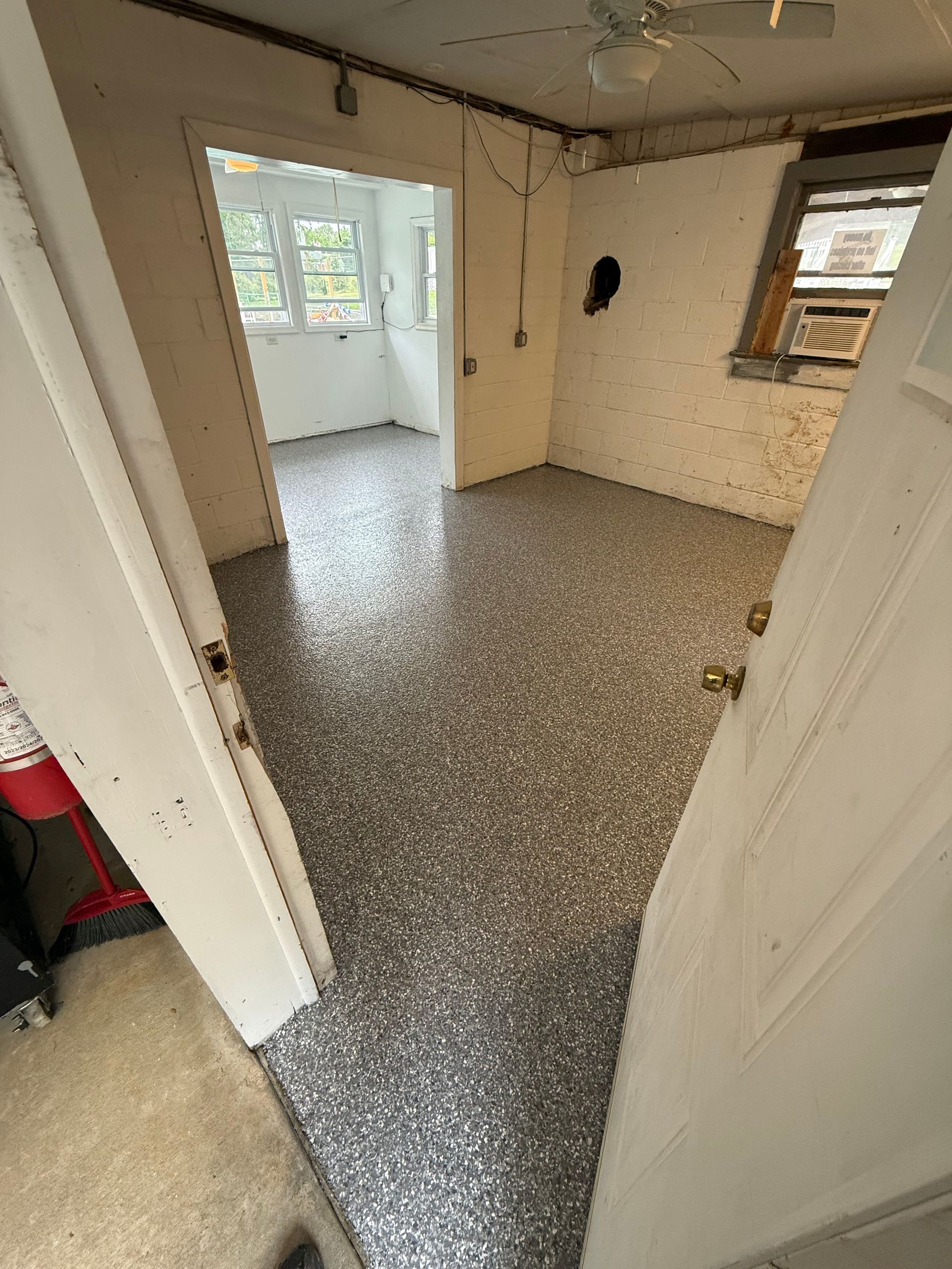 Empty room with speckled floor, white walls, open doorway, and windows letting in daylight