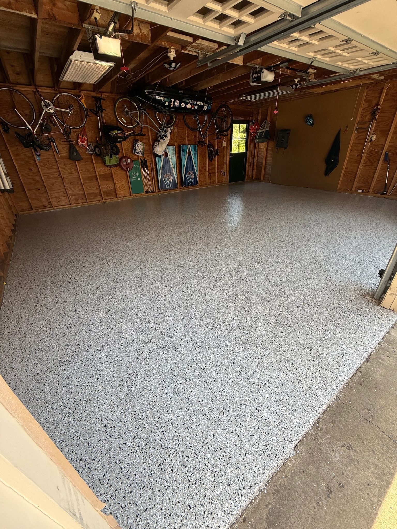 Empty garage interior with a speckled gray floor and hanging tools on wood-paneled walls