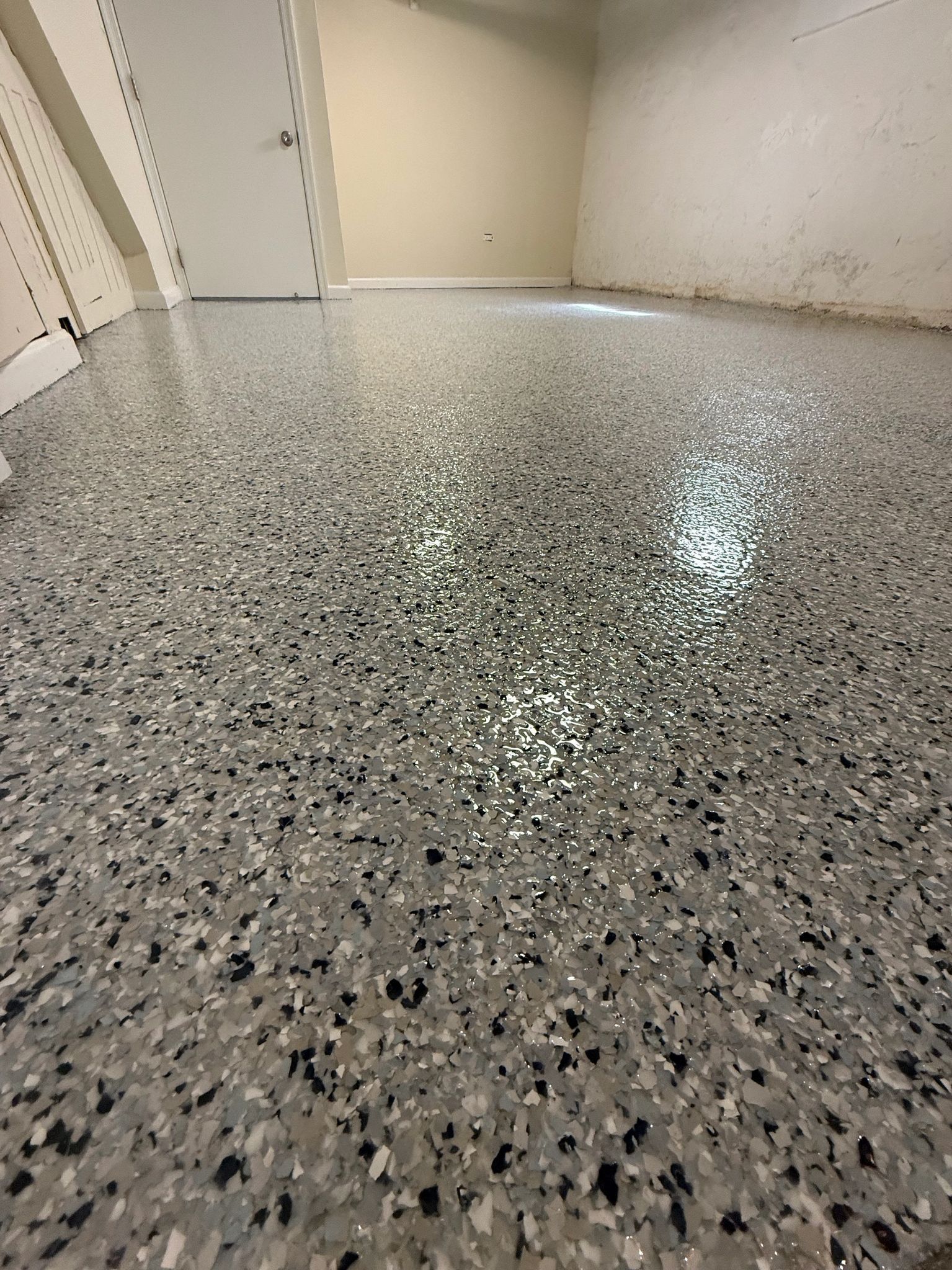 Speckled gray epoxy floor in a narrow hallway with white walls and a doorway.