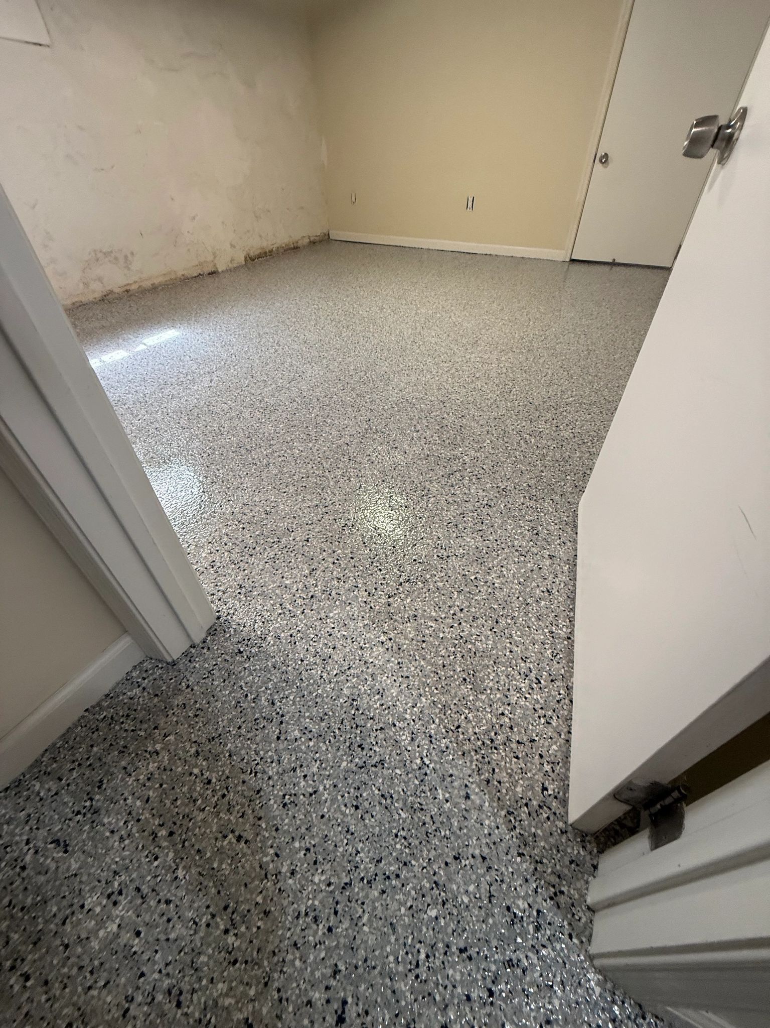 Empty room with speckled gray floor and beige walls, viewed from a doorway.