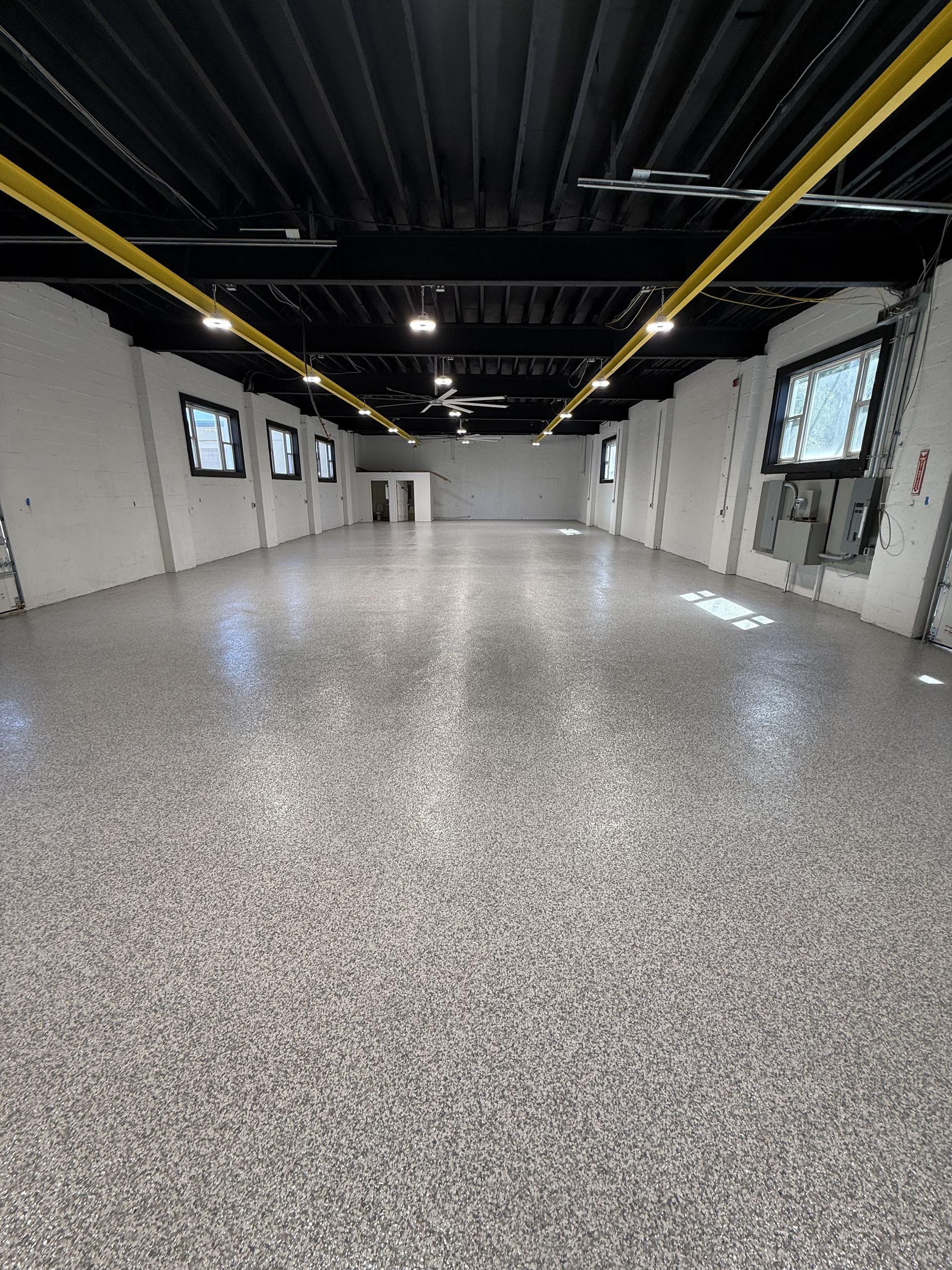 Empty modern room with speckled floor, white walls, black ceiling, and windows along both sides