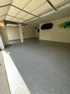 Empty garage with gray floor, open door, white walls, and a mounted black case on the right wall