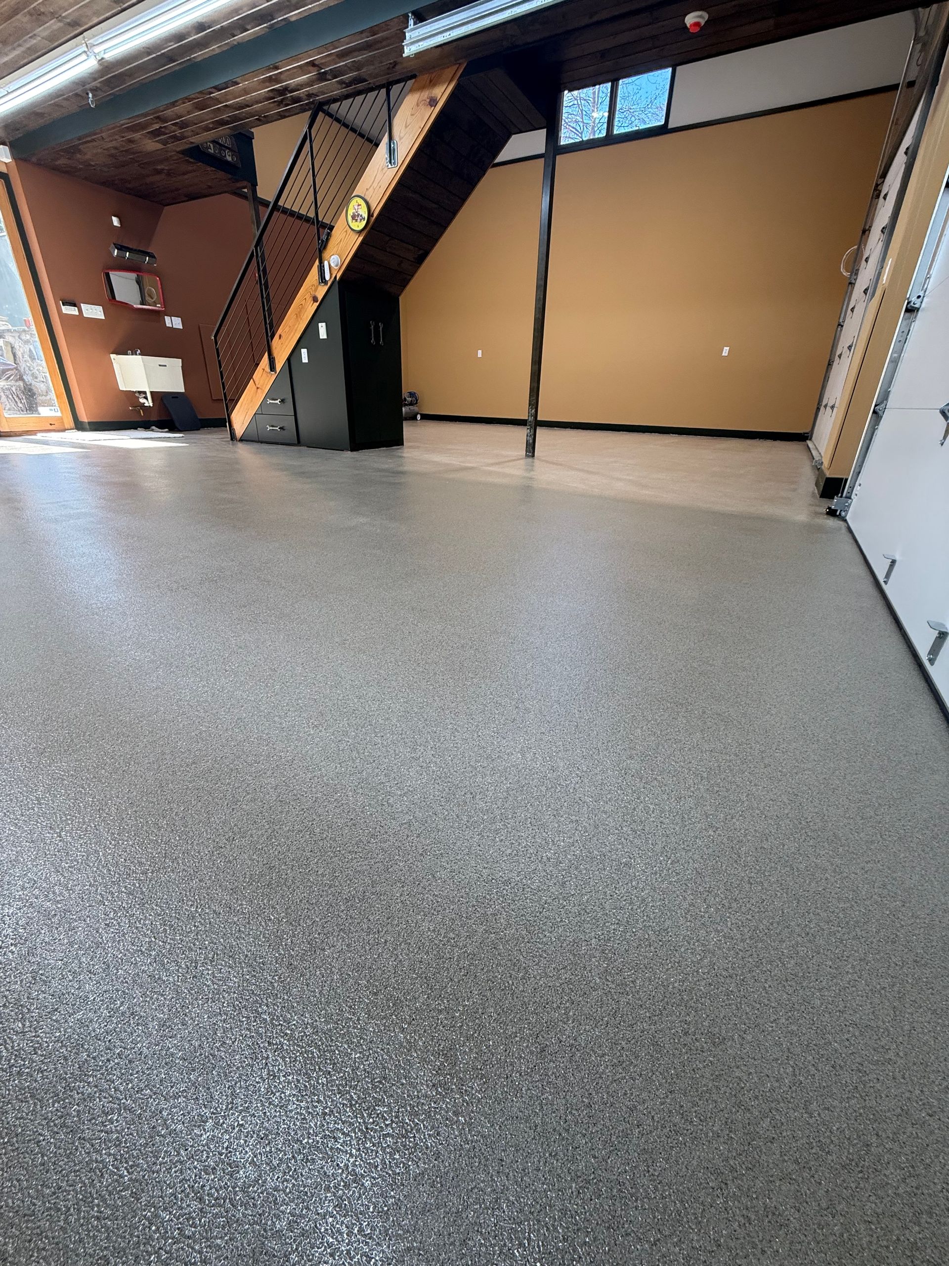 Empty indoor warehouse with a speckled gray floor, beige walls, and exposed ceiling beams.