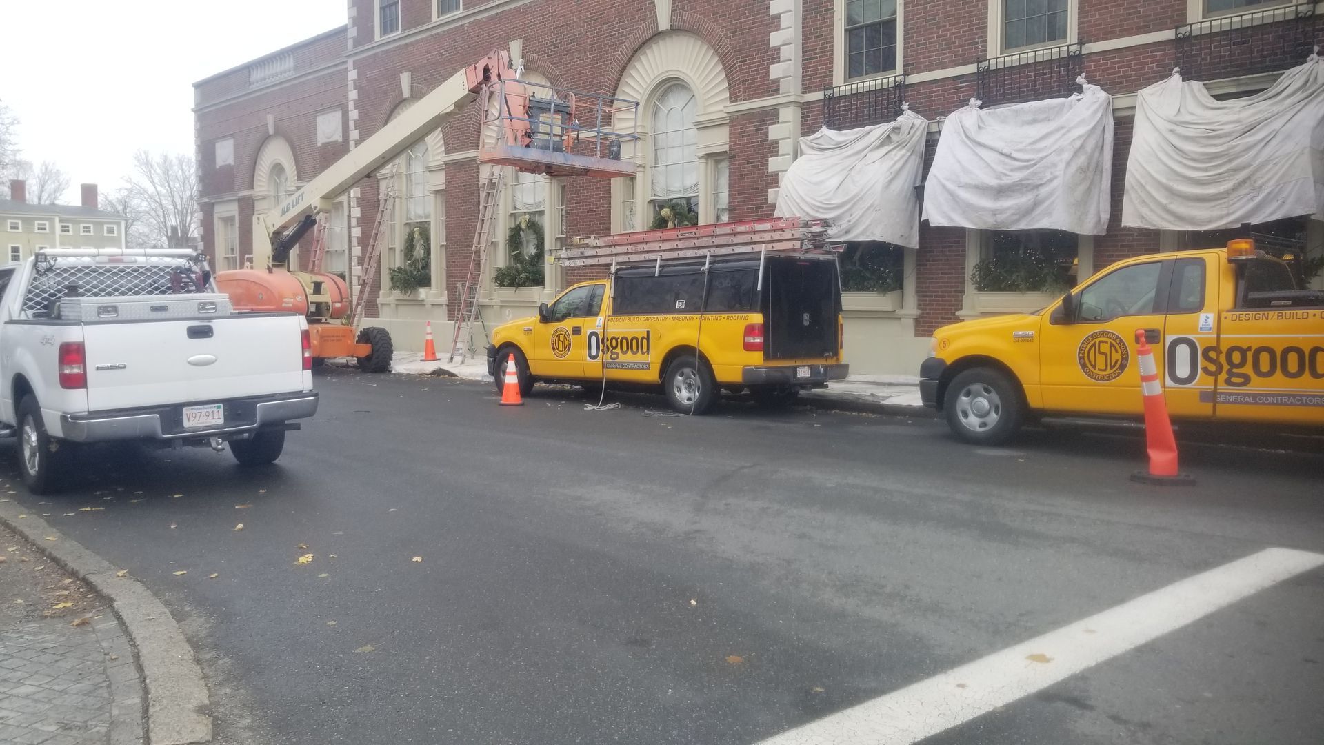 A yellow truck that says osgood is parked in front of a building.