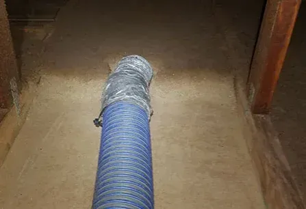 Blue flexible duct hose extending into a dusty room through a doorway