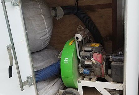 A green and black machine packed inside a storage compartment with bags and hoses around it