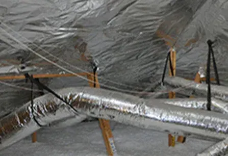 Foil-wrapped HVAC ducts in an unfinished attic with insulation and support straps