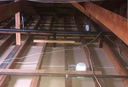 Attic with exposed wooden rafters, beams, and hanging wires above a partially finished floor