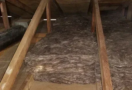 Attic with exposed wooden beams and insulation spread across the floor between joists