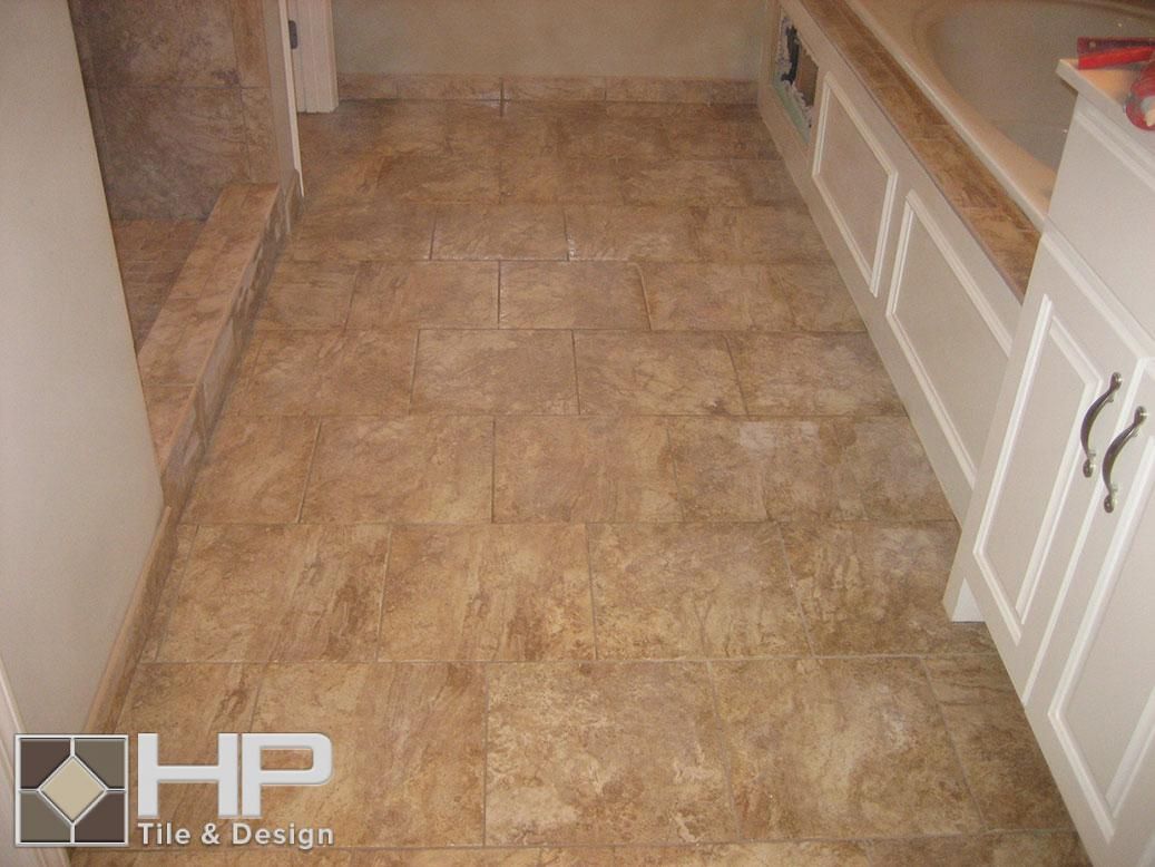 Bathroom floor with brown tiles, white cabinets and tub surround