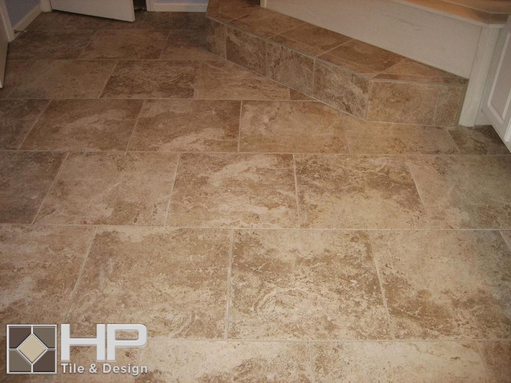 Bathroom floor with light-colored stone tiles and a darker, patterned inset rug design