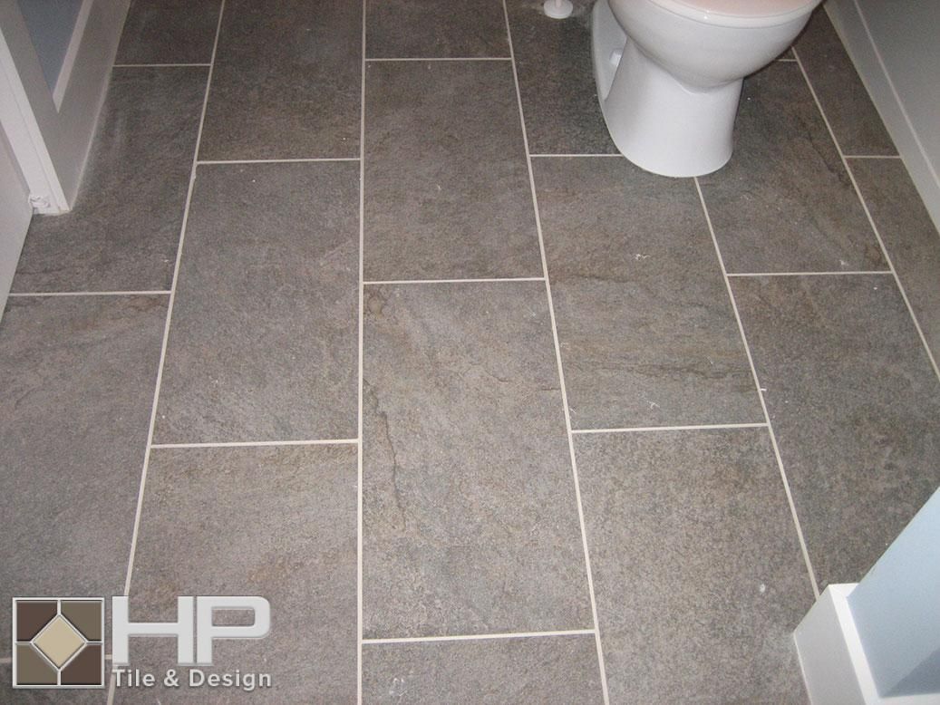 Gray rectangular floor tiles with white grout in a bathroom next to a toilet