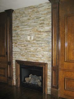 Fireplace with stone tile surround, wooden mantel and trim, set between wood paneling.