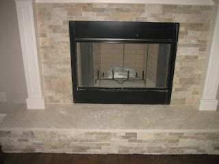 Fireplace with light-colored stone surround, black firebox, and white trim against a wall.