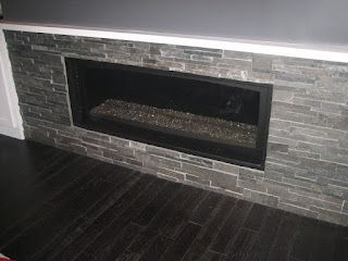 Fireplace built into a gray stone wall, with dark hardwood flooring.