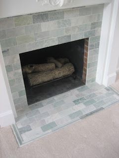 Fireplace with pale green-tiled surround and hearth, logs inside the opening, set in a white-painted wall.