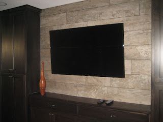 Black TV on a stone wall, dark cabinet, brown vase.