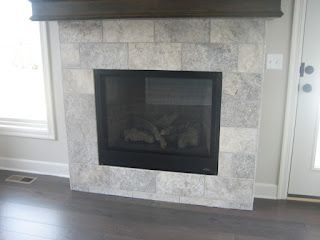 Fireplace with light gray stone tile surround, black firebox, dark wood mantel.