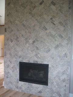 Fireplace with black insert, surrounded by gray and blue herringbone patterned tiles.