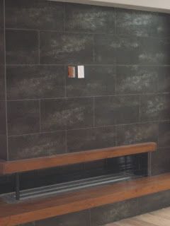Dark tiled wall with a wooden bench in front of a fireplace, and electrical outlets visible.