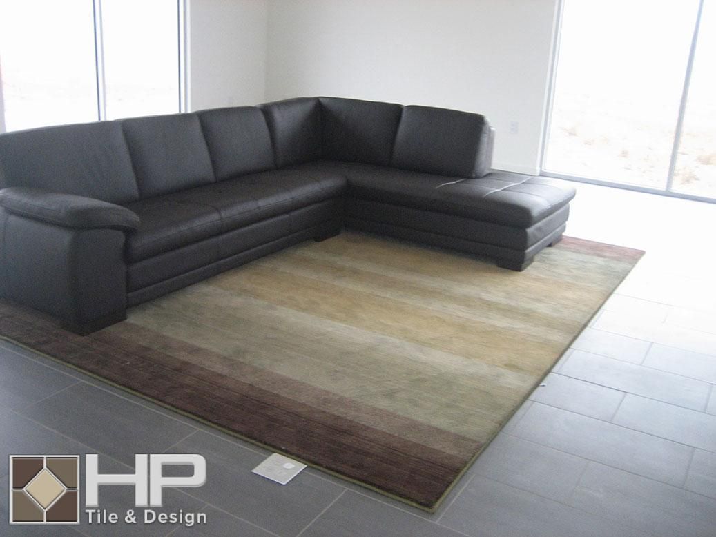 Dark leather sectional sofa on a rug with brown and beige tones, in a room with large windows