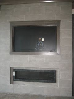 Gray tiled wall with recessed TV space framed in wood and a lower recessed fireplace.