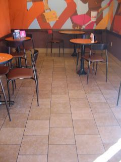 Cafe interior with orange tables, brown chairs, tiled floor, and a mural on the wall.