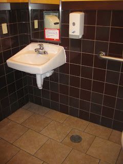 Accessible public restroom with a wall-mounted sink, soap dispenser, mirror, and grab bar