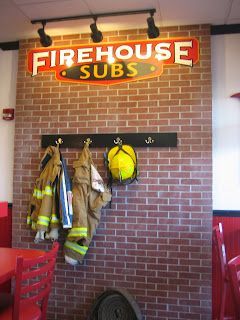 Firehouse Subs sign above a brick wall with firefighter gear hanging from a rack.