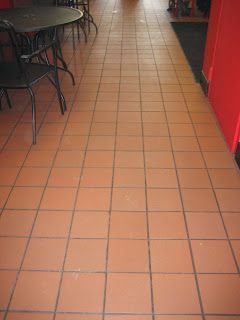 Terracotta tile floor in a restaurant setting, with tables and chairs visible on the left and a red wall on the right.