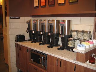 Coffee station with multiple urns, a microwave, and condiment cups.