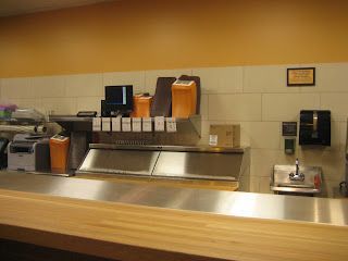 Counter with food service equipment against a tiled wall, orange and light colors.