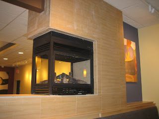 A three-sided fireplace encased in light brown tiles within a restaurant setting.