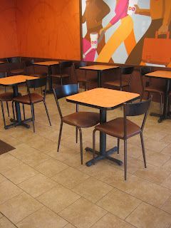 Empty cafe seating area; orange walls, brown tables and chairs, colorful mural.