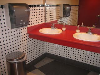 Bathroom with red countertop, two sinks, mirror, and black and white tiled walls.