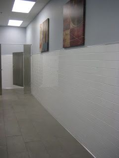 Public restroom hallway with white tiled walls, stainless steel stall dividers, and art.