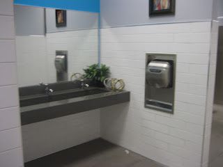 Public restroom with a sink, mirror, and hand dryer. White tiled walls.