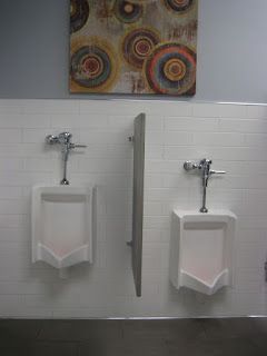 Two urinals with a privacy divider in a public restroom, beneath abstract artwork.