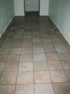 Brown tile floor in a room with white walls and a doorway at the end.