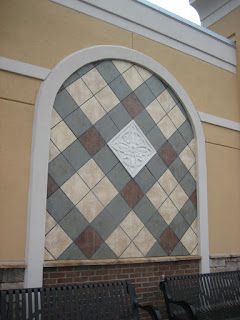 Arched wall decor with a diamond tile pattern in shades of gray, tan, and brown; centered white emblem.