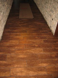 Wooden-planked floor in a narrow passage with white stone walls; a brown mat at the end.