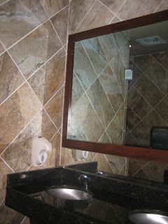 Bathroom with dark granite countertop, sinks, a mirror, and tiled walls. A soap dispenser is on the left.